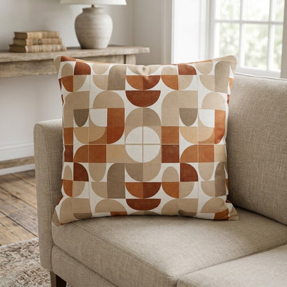 A square throw pillow with a mid-century modern geometric pattern in terracotta, tan, and cream, resting on a beige fabric sofa in a bright living room.