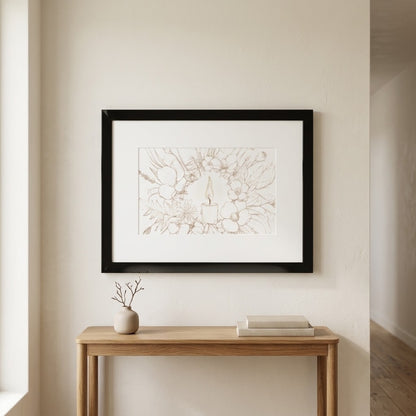 A framed art print featuring a delicate line drawing of a candle surrounded by wildflowers, displayed on a beige wall above a light wood console table with a small vase and books.