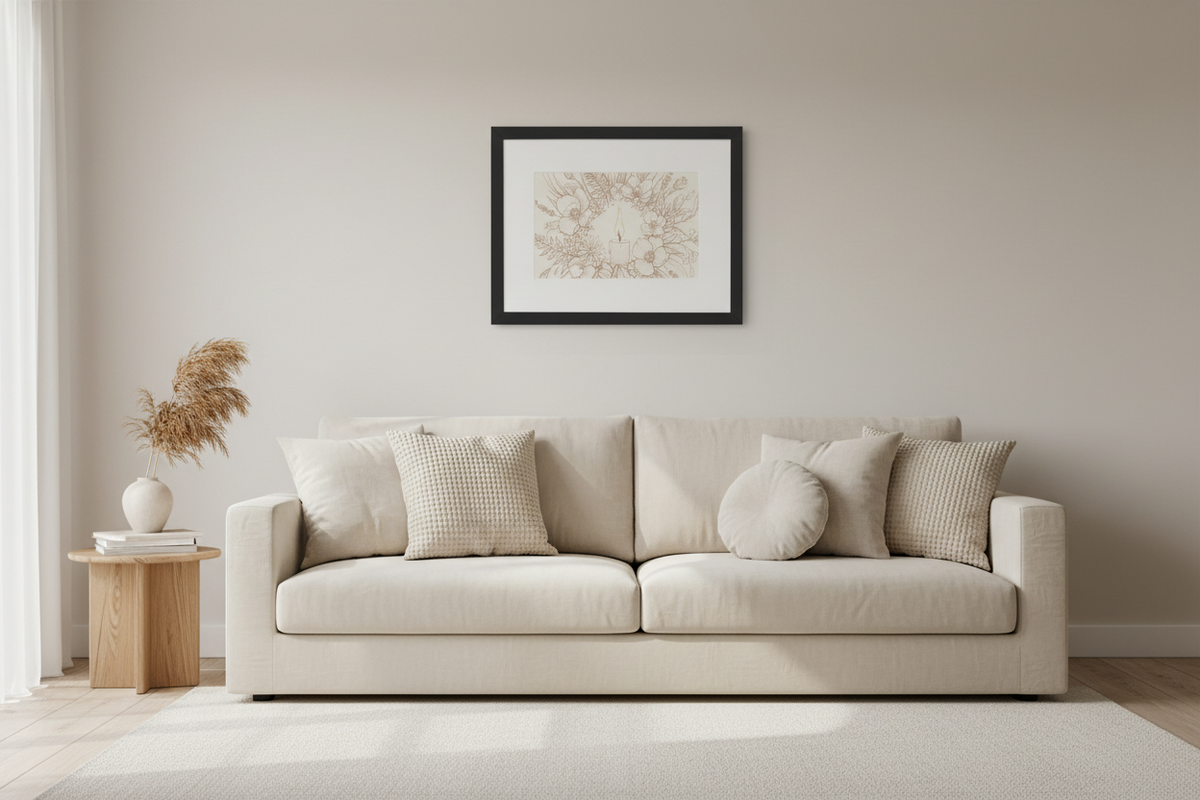 A modern beige fabric sofa with matching throw pillows in a minimalist living room setting, featuring a black-framed art print on the wall above it.